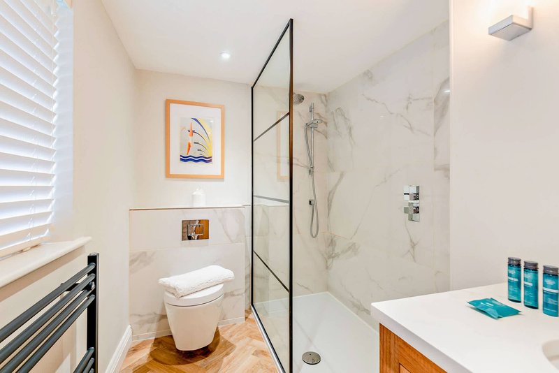 Modern bathroom with marble tiles, glass shower enclosure, white toilet, and wooden vanity