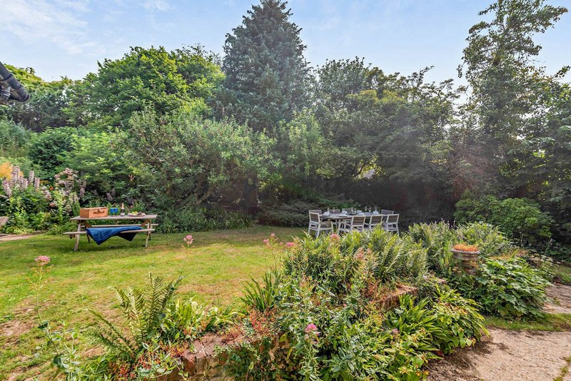 Garden with lawn, flowering plants, trees, blue boat and white seating area