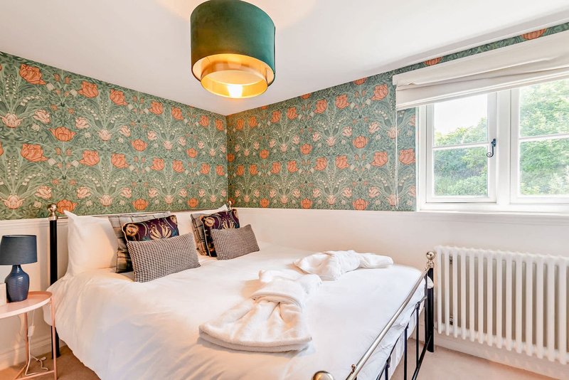 Bedroom with double bed, patterned wallpaper, green pendant light and window