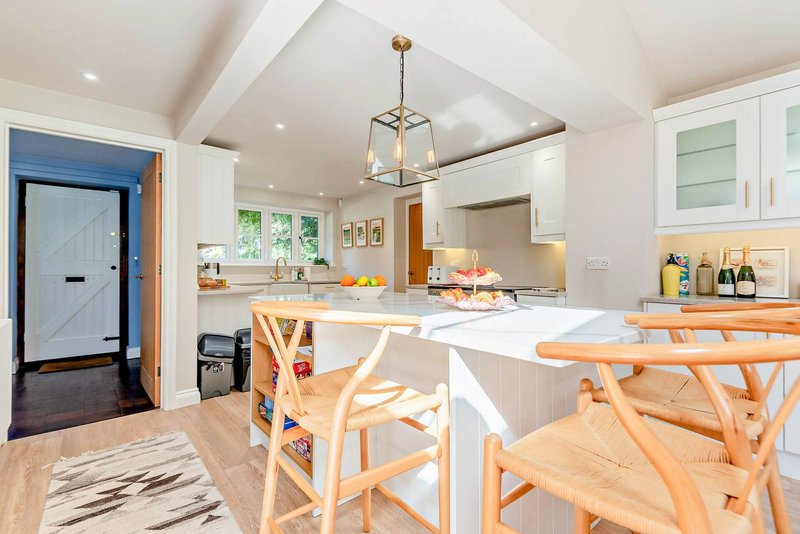 Bright open-plan kitchen and dining area with wooden chairs, white cabinetry, island counter and pendant lighting