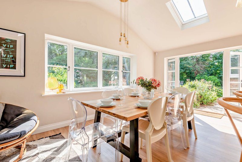 Bright dining room with wooden table, clear chairs, and garden views through large windows