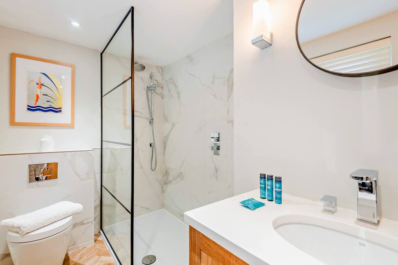 Modern bathroom with walk-in shower, white marble tiles, vanity sink and toilet