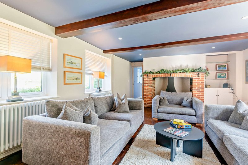 Spacious living room with multiple grey sofas, fireplace, wooden beams and natural light from windows