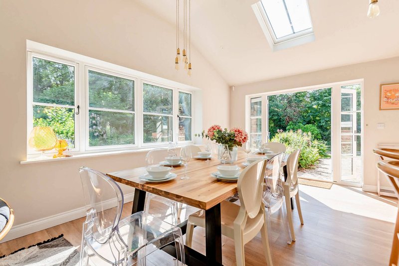Bright dining room with wooden table, clear chairs, large windows overlooking garden
