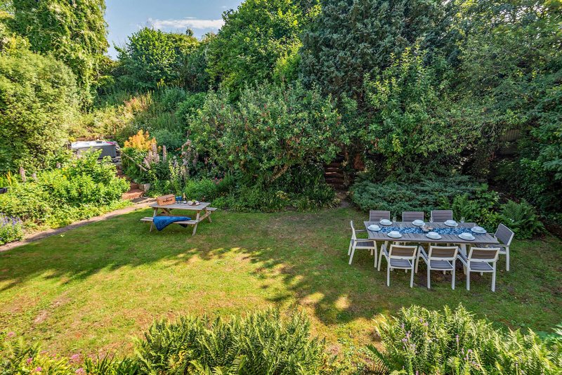 Garden with lawn, dining table setup, chairs, trees and blue lounger