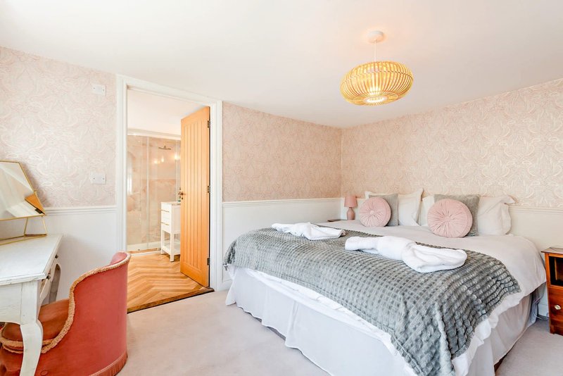 Bedroom with double bed, pink cushions, grey bedding, wooden door and en-suite bathroom visible