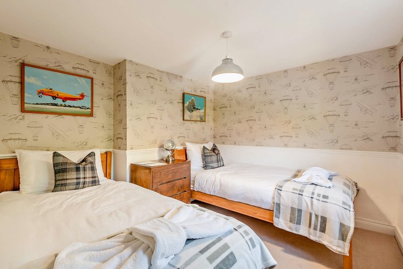 Twin bedroom with wooden beds, plaid cushions, framed artwork and pendant light