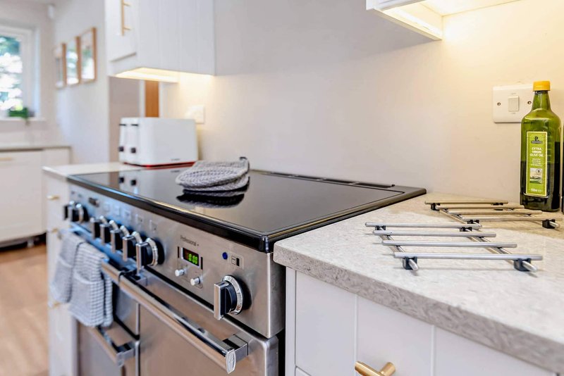 Modern kitchen with black stovetop, marble countertop, white cabinetry and olive oil bottle