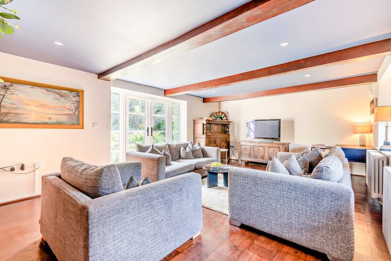 Spacious living room with two upholstered sofas, wooden beams, large windows and hardwood flooring