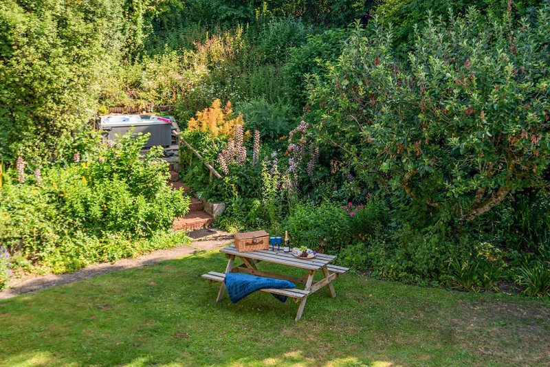 Garden with picnic table, blue cushion, and lush green vegetation surrounding property