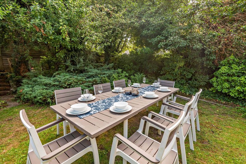Garden dining table set with place settings and chairs surrounded by mature trees