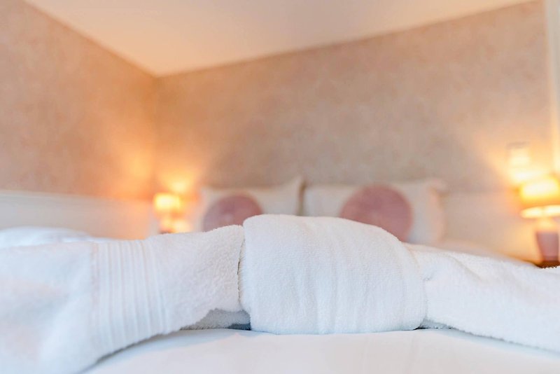 Bedroom with white pillows, rumpled bedding, warm ambient lighting, and headboard