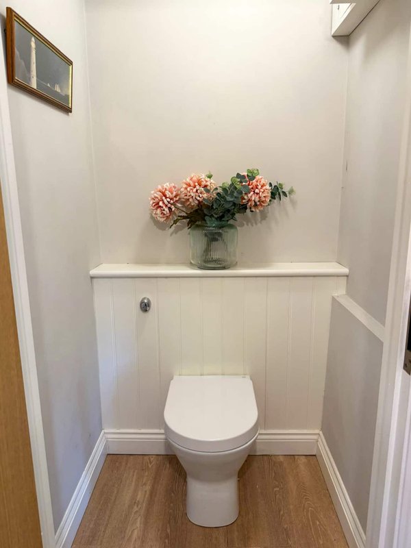 Small bathroom with toilet, white storage cabinet, and pink flowers in vase