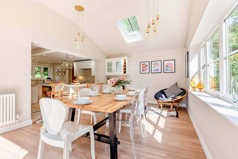 Open-plan dining and kitchen area with wooden table, white chairs, and pendant lighting