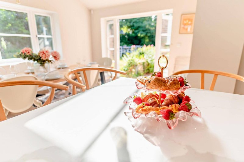 Bright dining room with wooden chairs, white table, fruit bowl and garden views