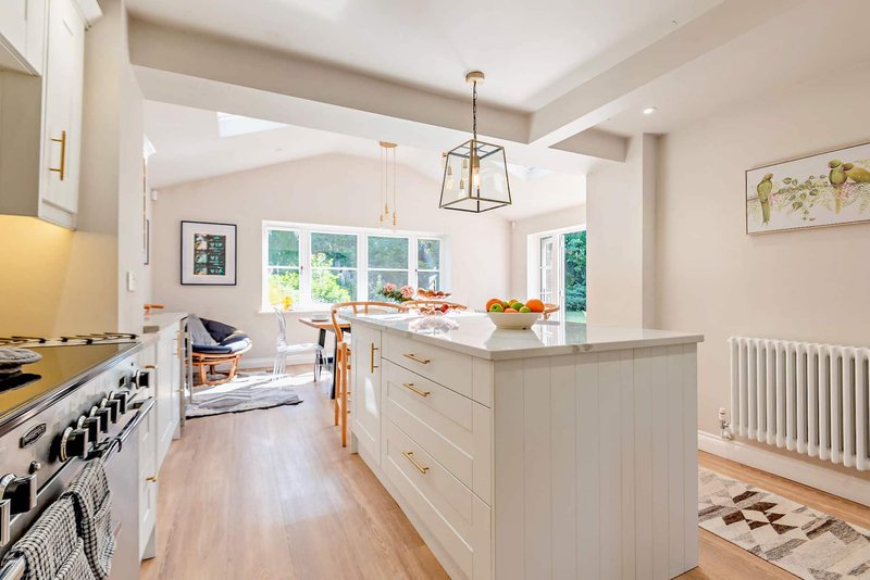 Modern kitchen with white cabinetry, island, pendant lighting and large windows overlooking garden