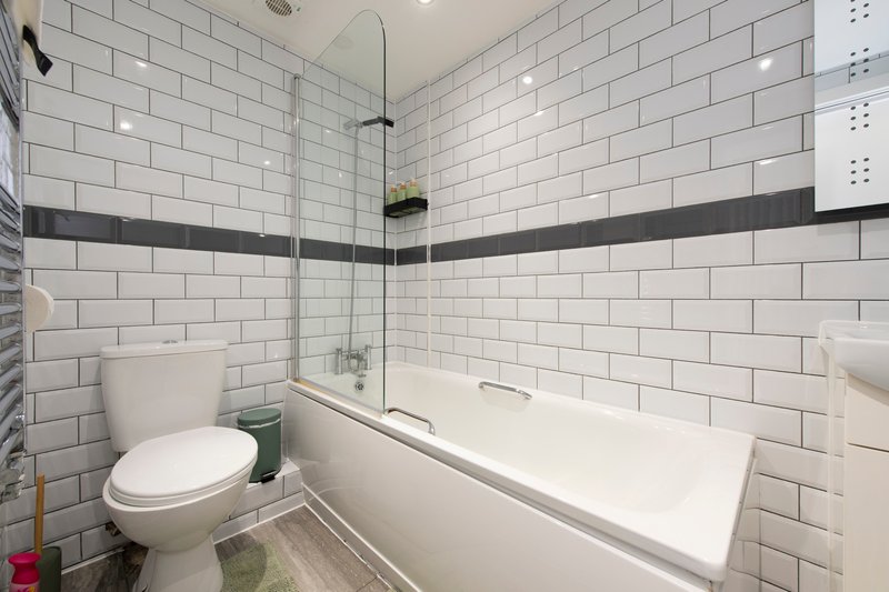 Modern bathroom with white subway tile, bathtub, toilet, and glass shower enclosure