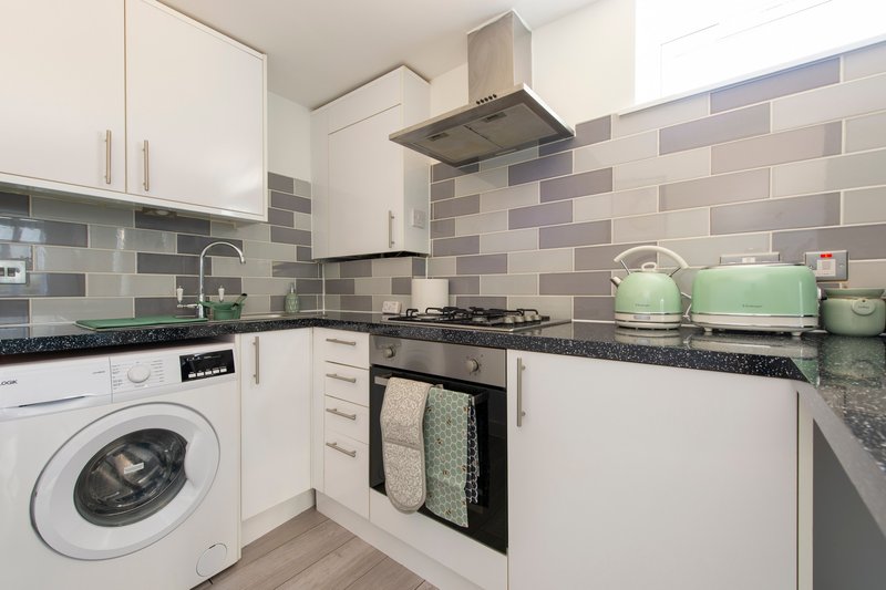 Modern kitchen with white cabinets, gray tile backsplash, gas range, washing machine and granite countertops
