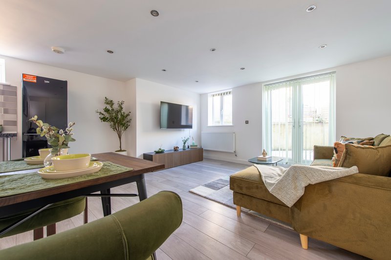 Open-plan living room with seating, dining table, wall-mounted TV and patio doors