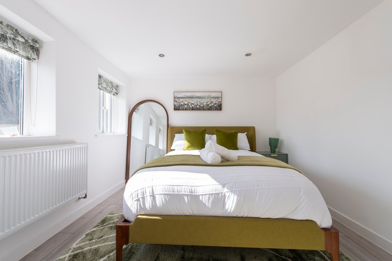 Bright bedroom with double bed, olive green headboard, white bedding, and wooden frame