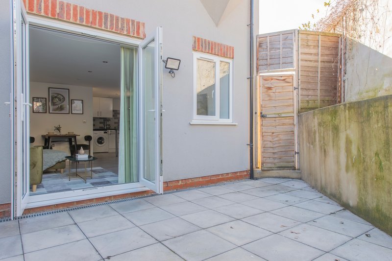 Patio area with sliding glass doors opening to bedroom, wooden fence and tiled flooring