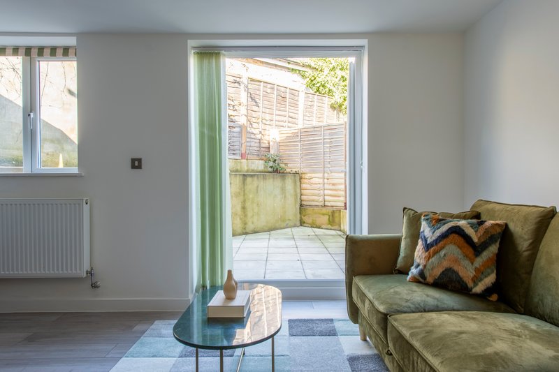 Bright living room with olive sofa, glass coffee table, and view to patio garden