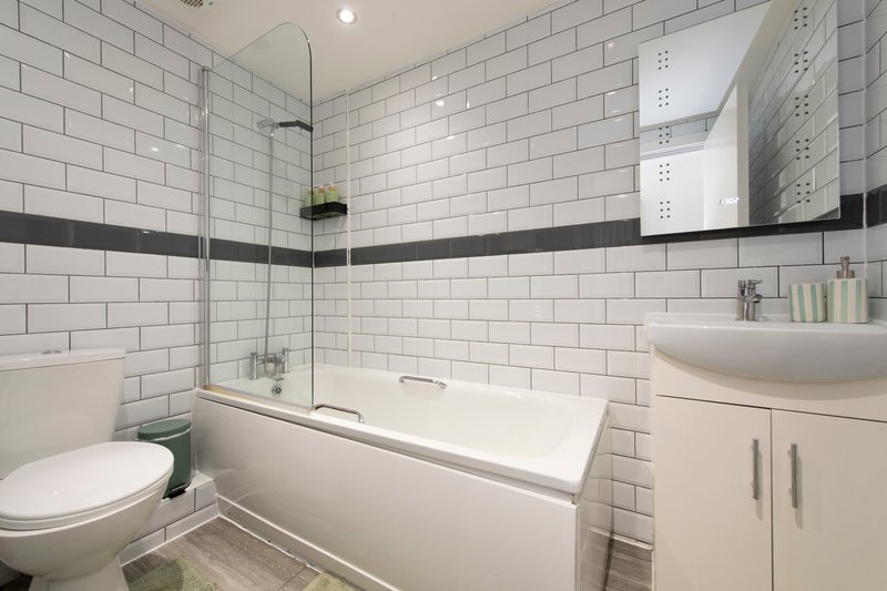 Modern bathroom with white subway tiles, bath tub, toilet, sink and mirrored cabinet