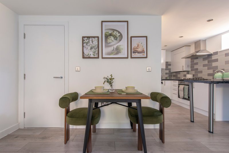 Open-plan dining and kitchen area with wooden table, green chairs, and framed wall art