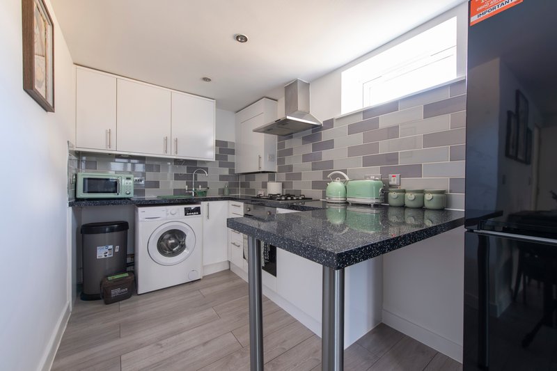 Modern kitchen with white cabinetry, black countertop, tiled backsplash, and integrated appliances