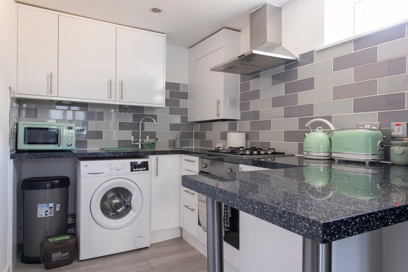 Modern kitchen with white cabinets, grey tile backsplash, black granite countertop, gas hob and extractor hood