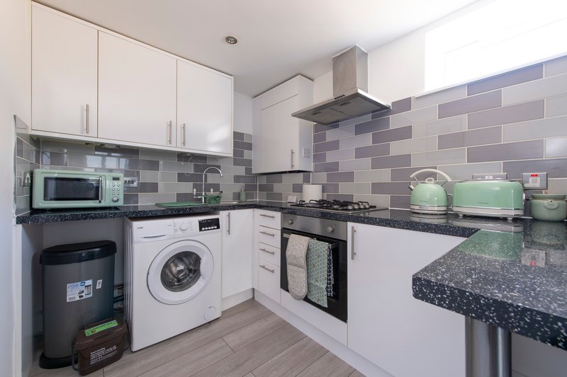 Modern kitchen with white cabinets, grey tile splashback, integrated appliances and black worktops