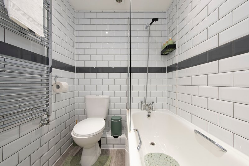 Modern bathroom with white subway tile, toilet, bathtub, shower, and heated towel rail