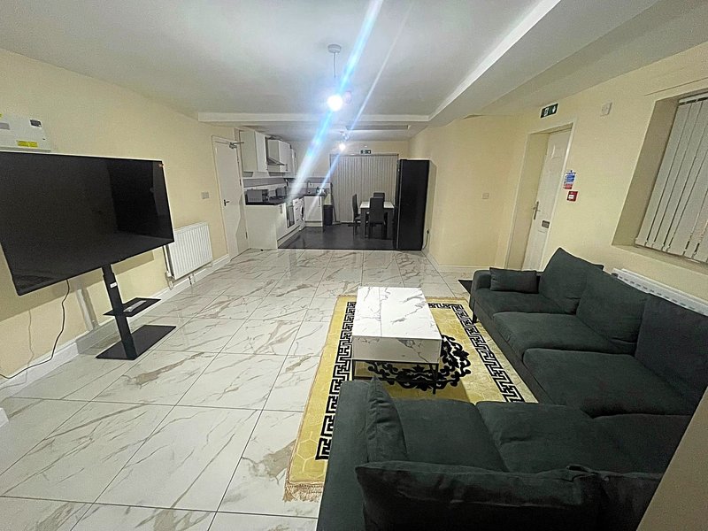 Spacious open-plan living area with dark sofa, marble flooring, wall-mounted TV and kitchen in background