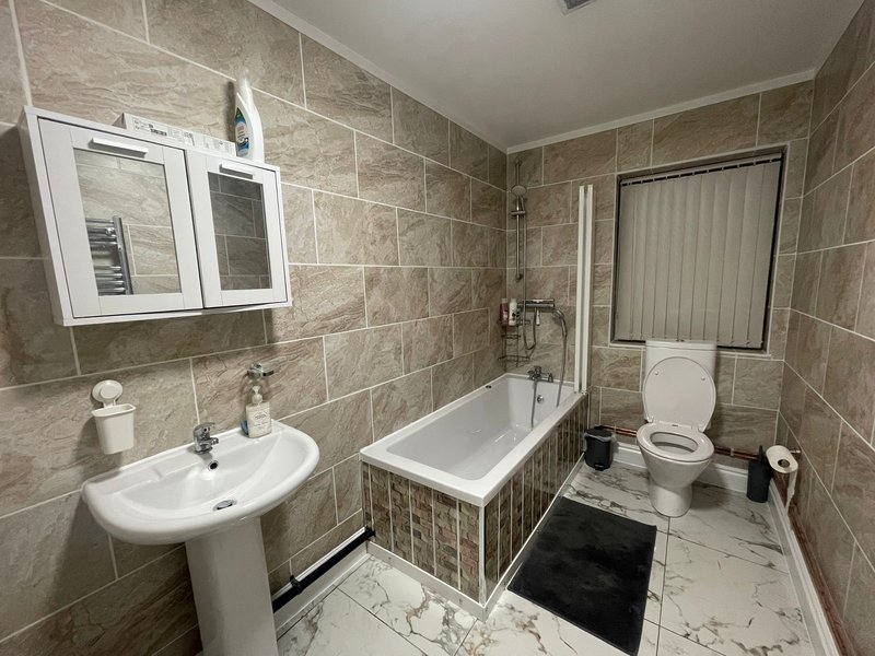 Bathroom with pedestal sink, bathtub, toilet, mirrored cabinet and tiled walls