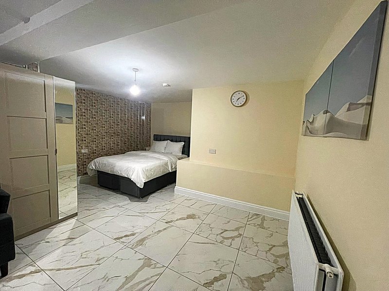 Spacious bedroom with double bed, marble-effect flooring, yellow walls and wall clock