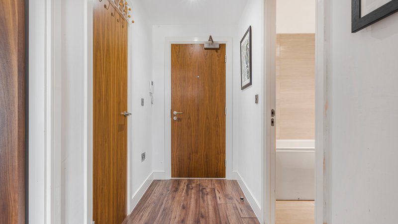 Hallway with wooden doors, white walls, wood-grain flooring, and framed wall art