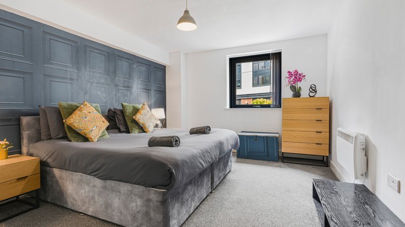 Modern bedroom with grey upholstered bed, wooden dresser, pendant light and window seat