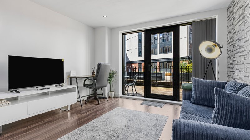 Modern living room with TV, blue armchairs, wooden floor and balcony doors