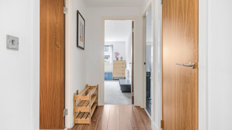Hallway with wooden doors, shoe rack, and view into open-plan living area