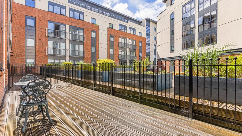 Modern apartment building exterior with shared courtyard, wooden deck, black metal railings and planters