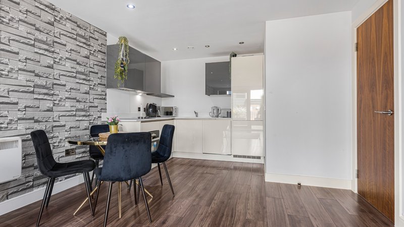 Open-plan kitchen and dining area with brick-effect wallpaper, white cabinetry, and dark dining table