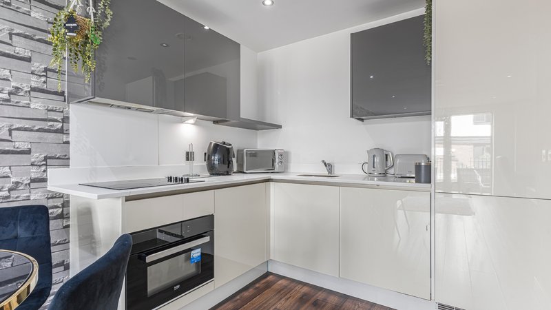 Modern white kitchen with grey upper cabinets, built-in oven, and wooden flooring