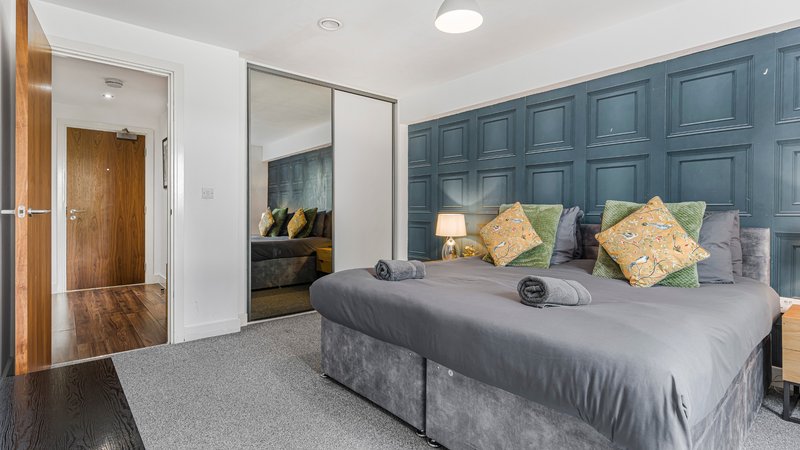 Modern bedroom with grey bed, blue panelled headboard, mirrored wardrobe and wooden door