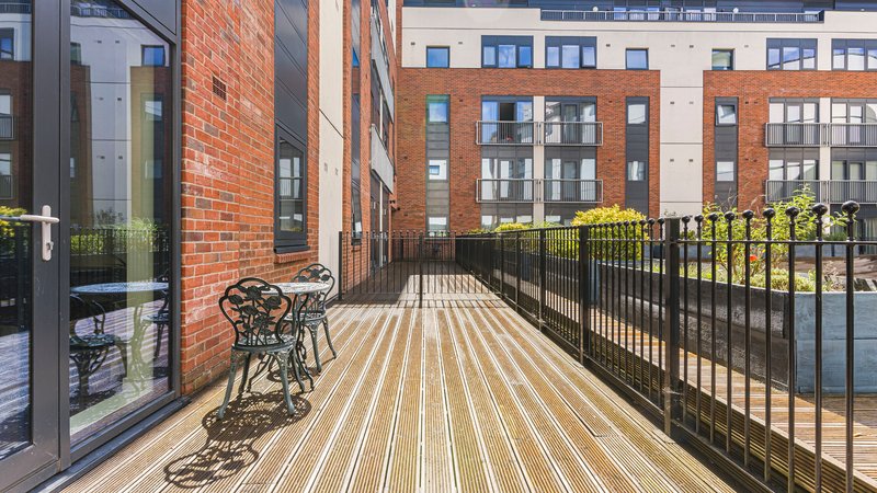 Wooden decked balcony with metal railing, bicycle, and urban brick building views
