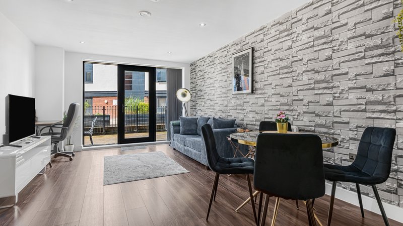 Modern open-plan living room with grey brick accent wall, black chairs, sofa and glass doors to balcony