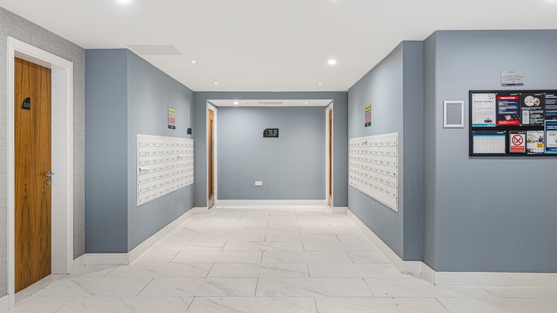 Modern hallway with blue-grey walls, light tile flooring, wooden door, and wall-mounted shelving
