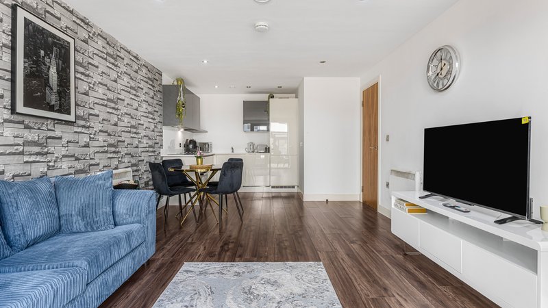 Modern open-plan living room with blue sofa, dining area, wooden floors and wall-mounted TV