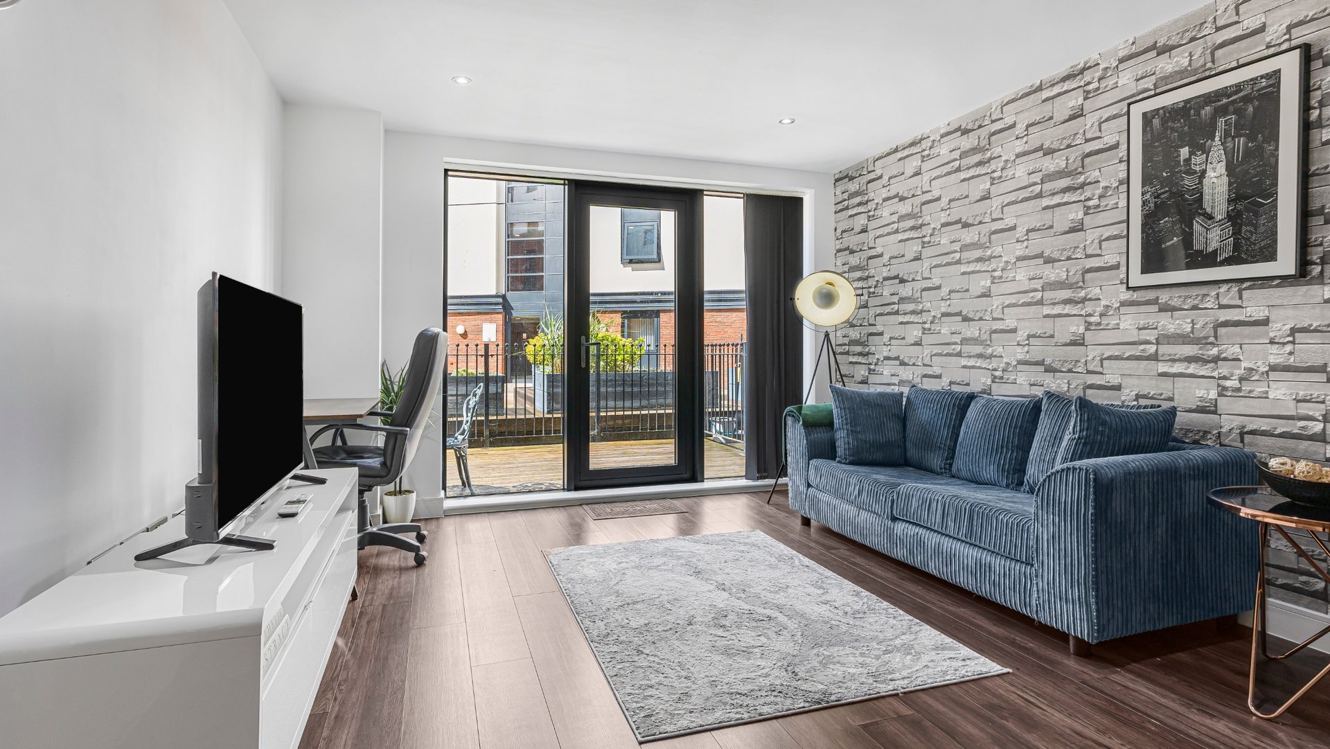Modern living room with blue sofa, TV, and patio doors leading to balcony