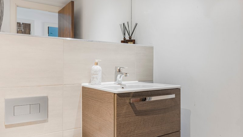 Modern bathroom with wooden vanity sink, white ceramic tiles, and minimalist decor