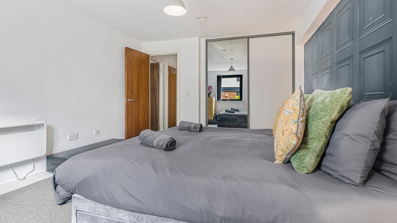 Bright bedroom with grey bed, colorful cushions, wooden door and built-in wardrobe